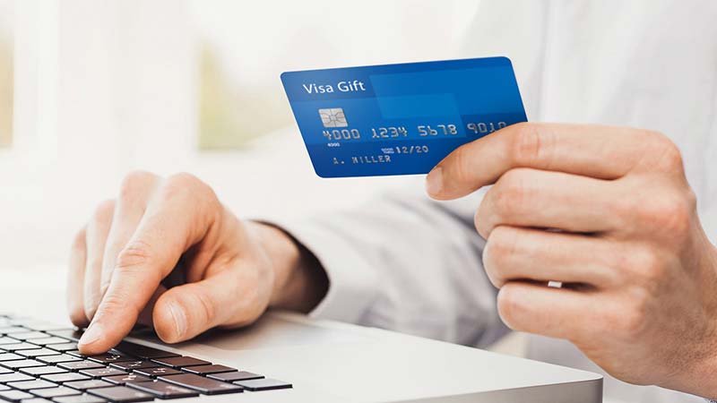 Person using a laptop and holding their Visa Gift Card.