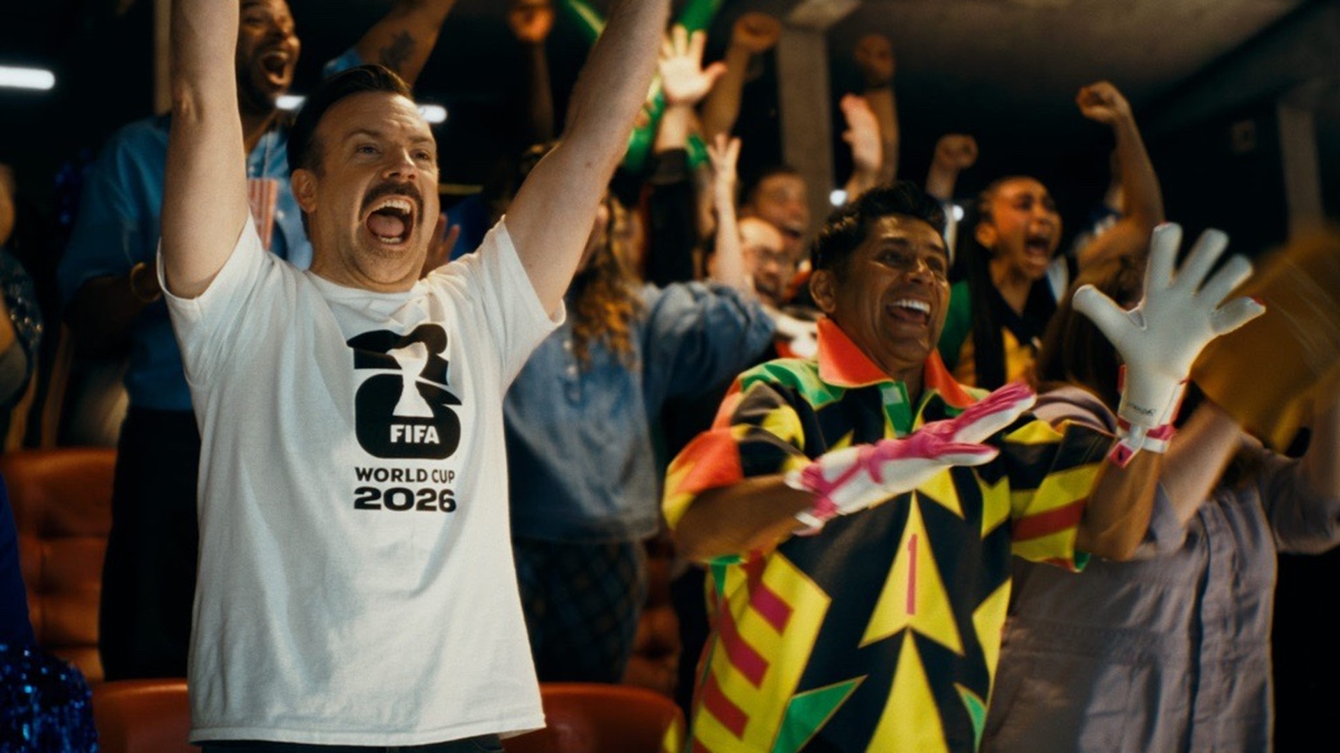 Jason Sudeikis celebrating wearing a T-shirt with the FIFA World Cup 2026 logo.