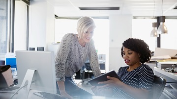 Solutions numériques Visa Two women at a desk looking at a tablet and discussing content on it.