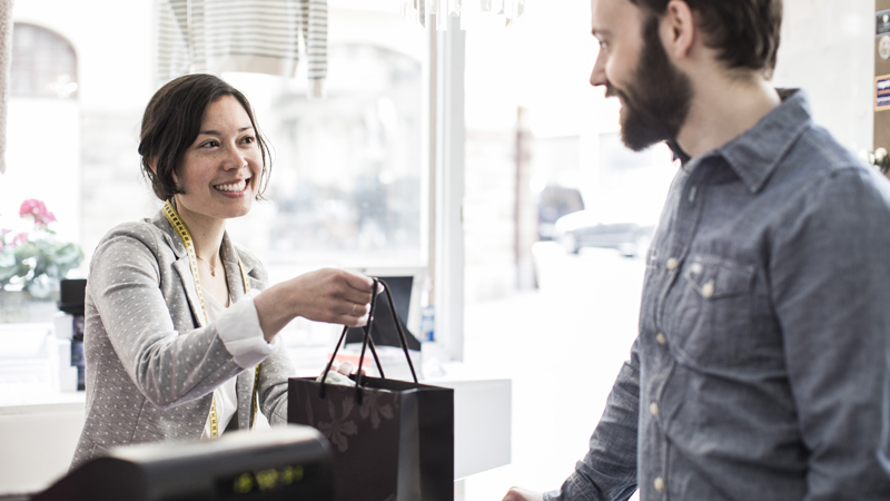 458003953 Female design professional giving a shopping bag to customer at cash counter in a studio space.