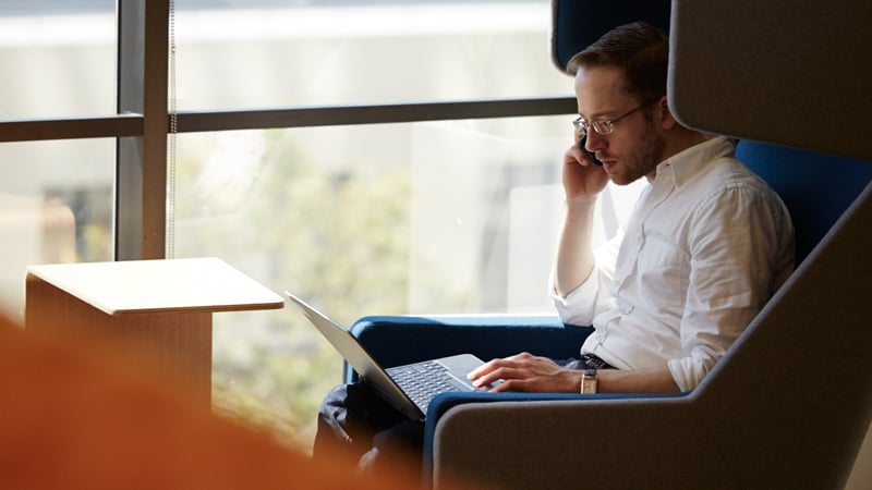 A man sitting in a chair using his mobile phone and laptop.