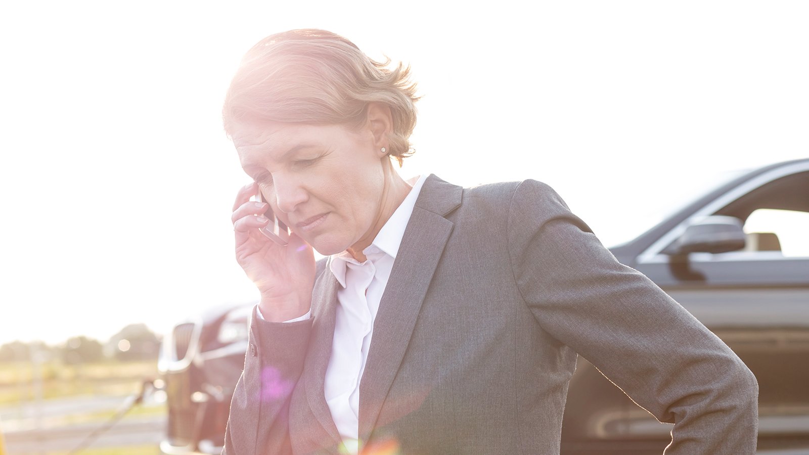 Woman standing at front of vehicle talking on mobile phone.