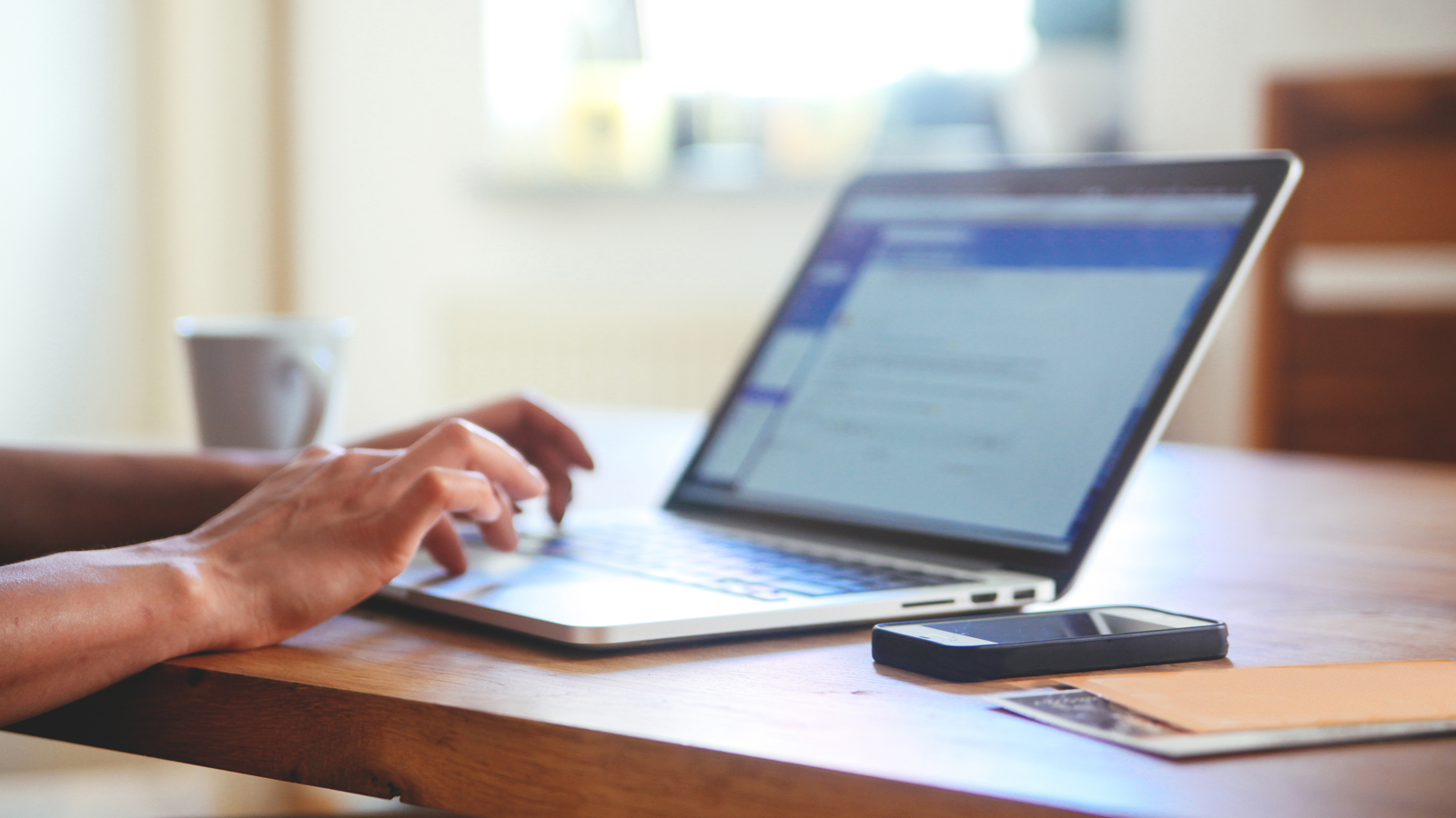 Person at table using a laptop with a smart phone, papers and coffee cup nearby. Person at table using a laptop with a smart phone, papers and coffee cup nearby.