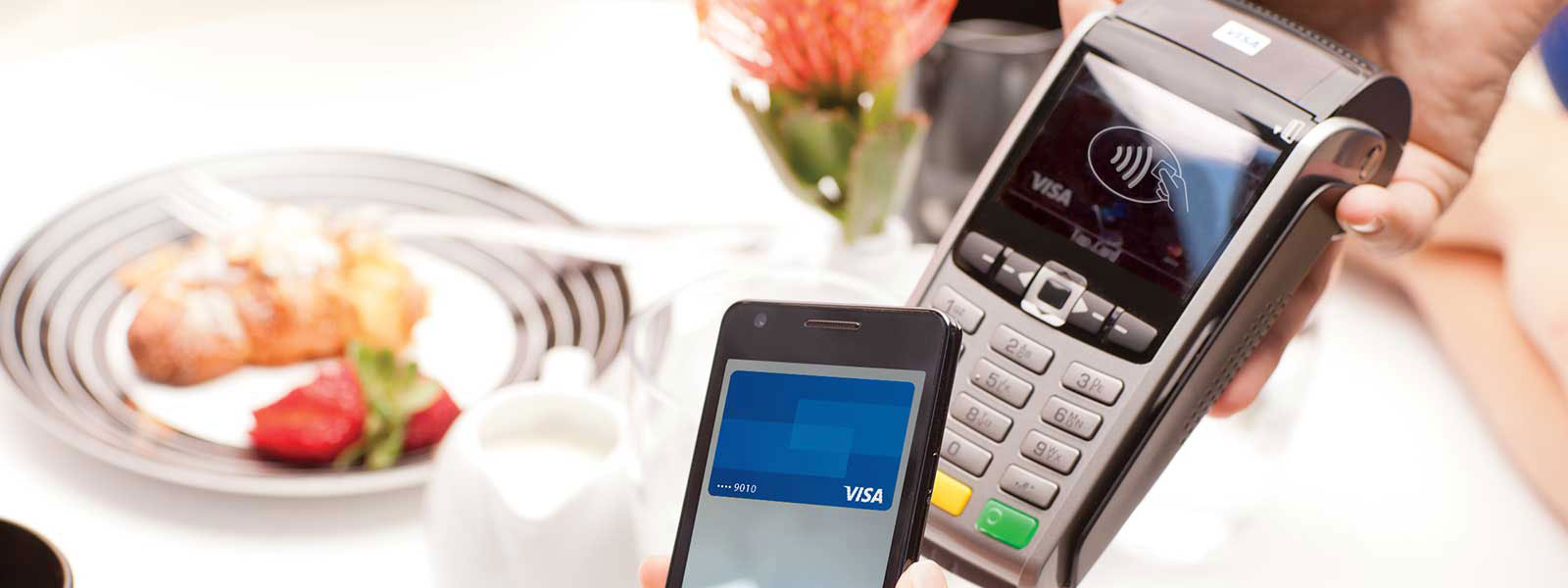 A mobile phone being held over a checkout terminal displaying the Contactless Symbol.