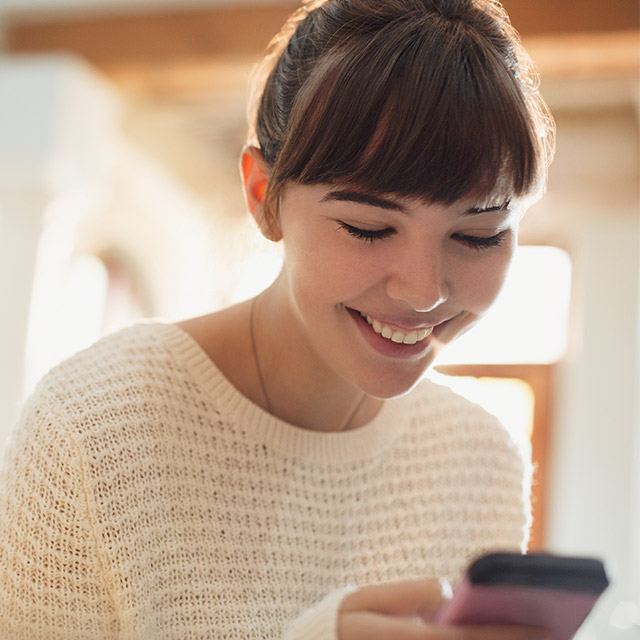 Une femme souriante en regardant son téléphone intelligent, faisant un paiement avec son appareil. 