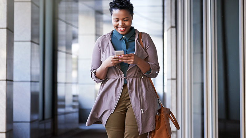 Une femme souriante regardant un téléphone intelligent.