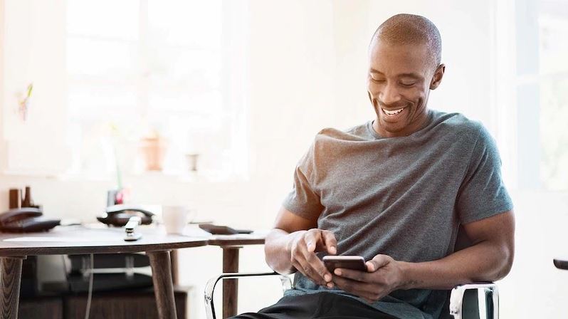 Man using his smartphone while sitting on a chair near a desk. Man using his smartphone while sitting on a chair near a desk.